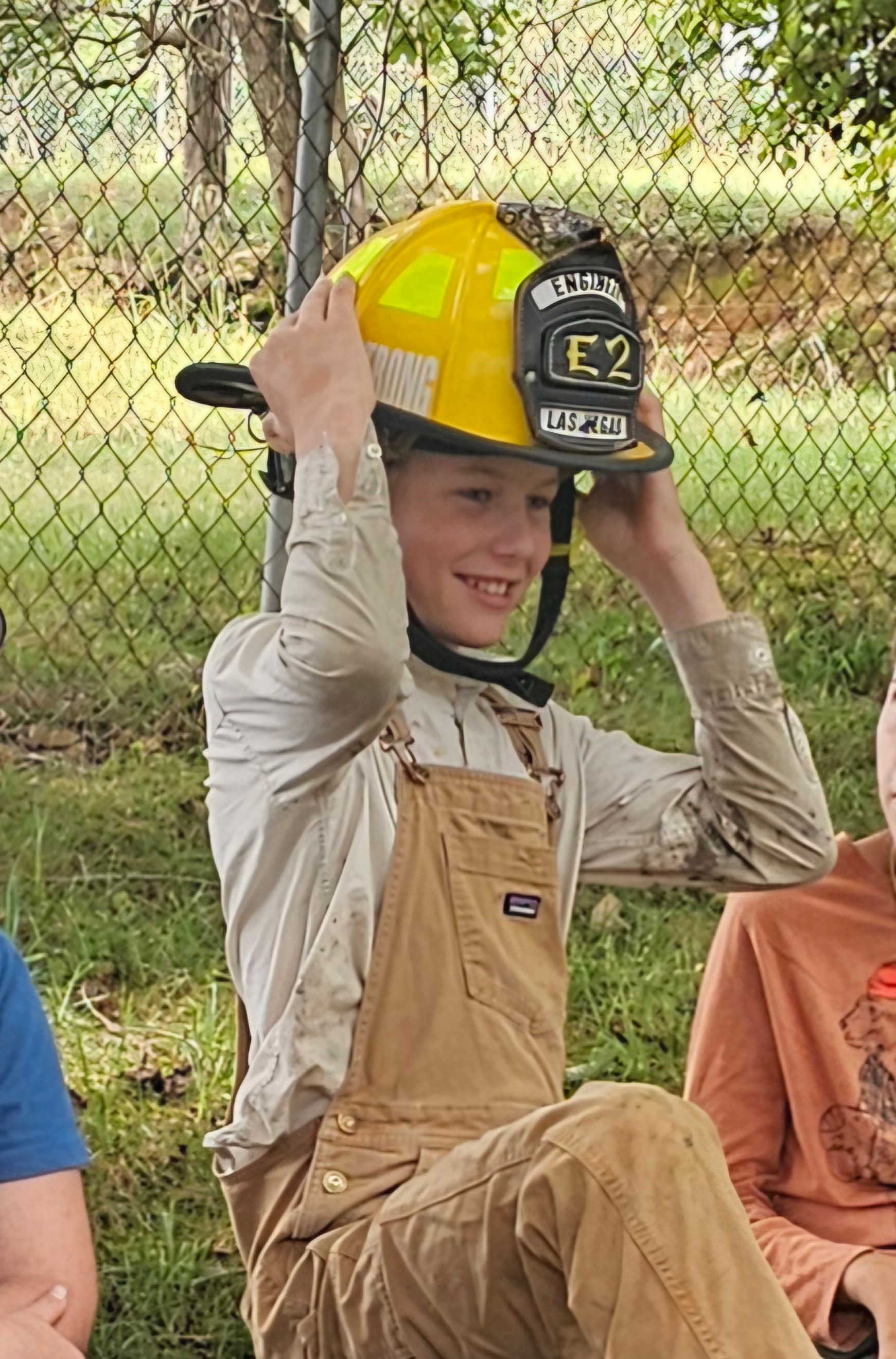 Student smiling while trying on a firefighter helmet outdoors