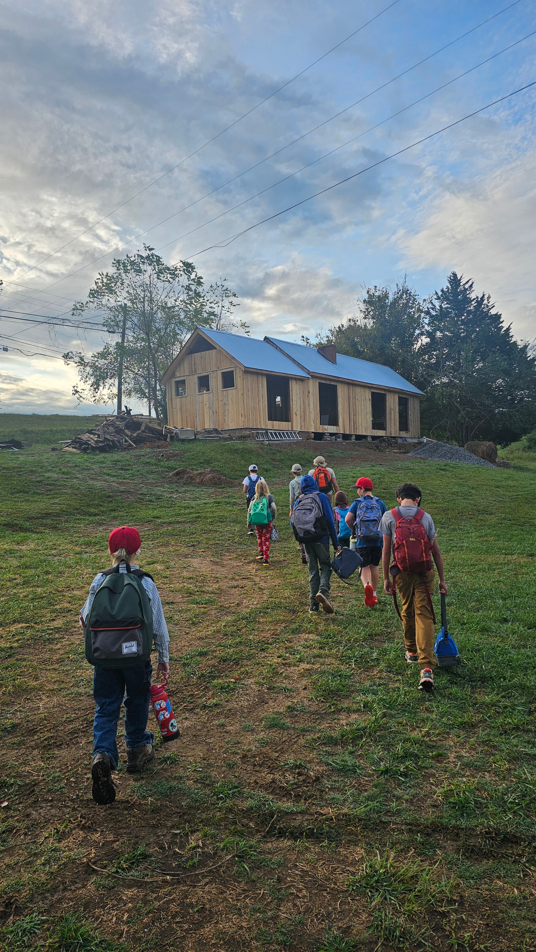 Students with backpacks walking across the farm field toward the barn